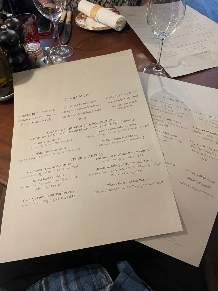 Two A3 sheets of off-white paper with a large-print menu. The top page has starters and light bites including Piggy Bites, vegetable dishes from the garden, greenhouse and polytunnel and other starters including venison carpaccio and cured black bream. The bottom sheet has mains including rump steak, lamb and monkfish.
